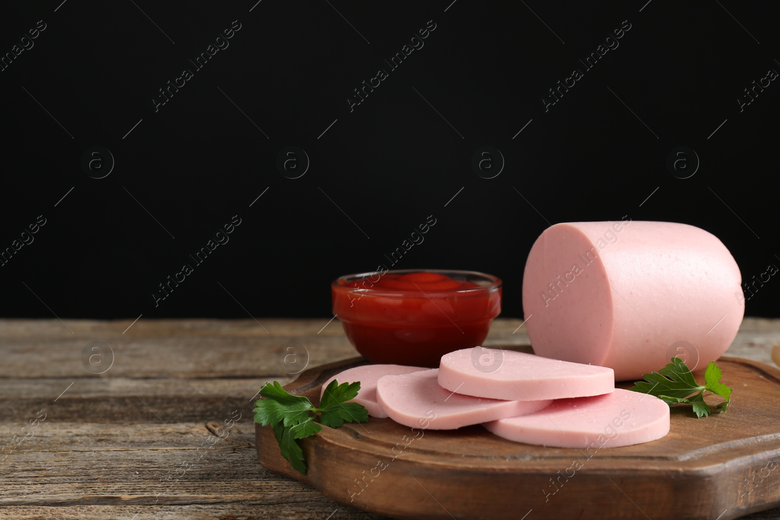 Photo of Tasty boiled sausage, ketchup and parsley on wooden table, space for text