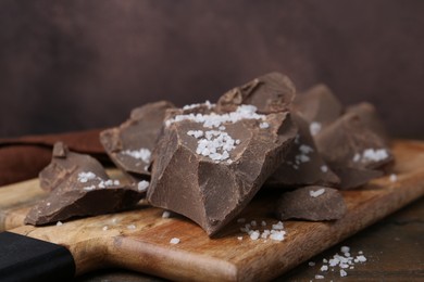 Pieces of chocolate with salt on wooden table, closeup