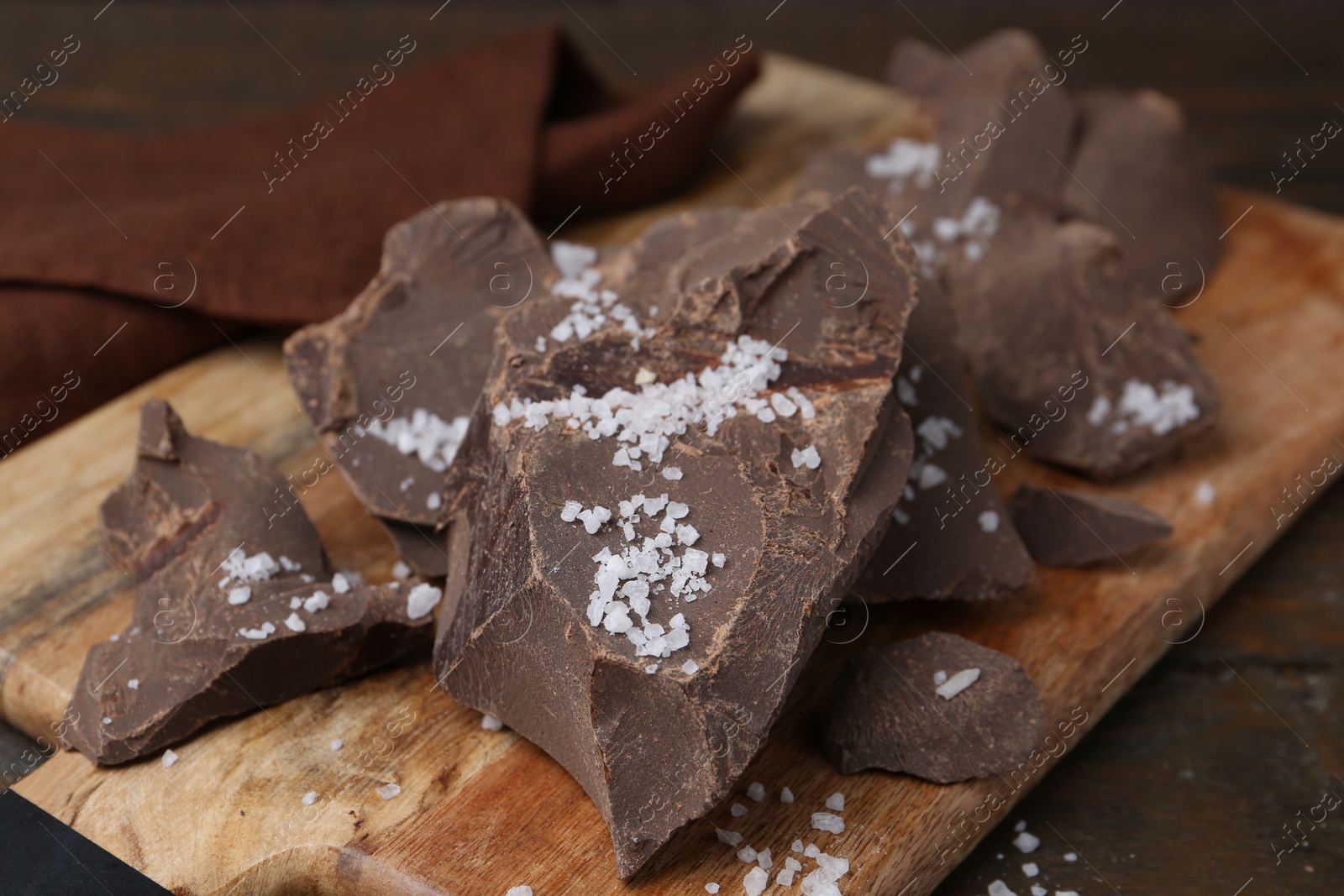 Photo of Pieces of chocolate with salt on wooden table, closeup