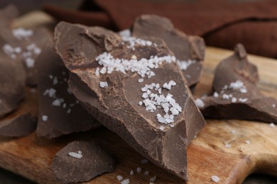 Photo of Pieces of chocolate with salt on wooden table, closeup