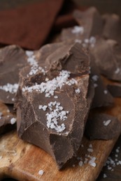 Photo of Pieces of chocolate with salt on wooden table, closeup