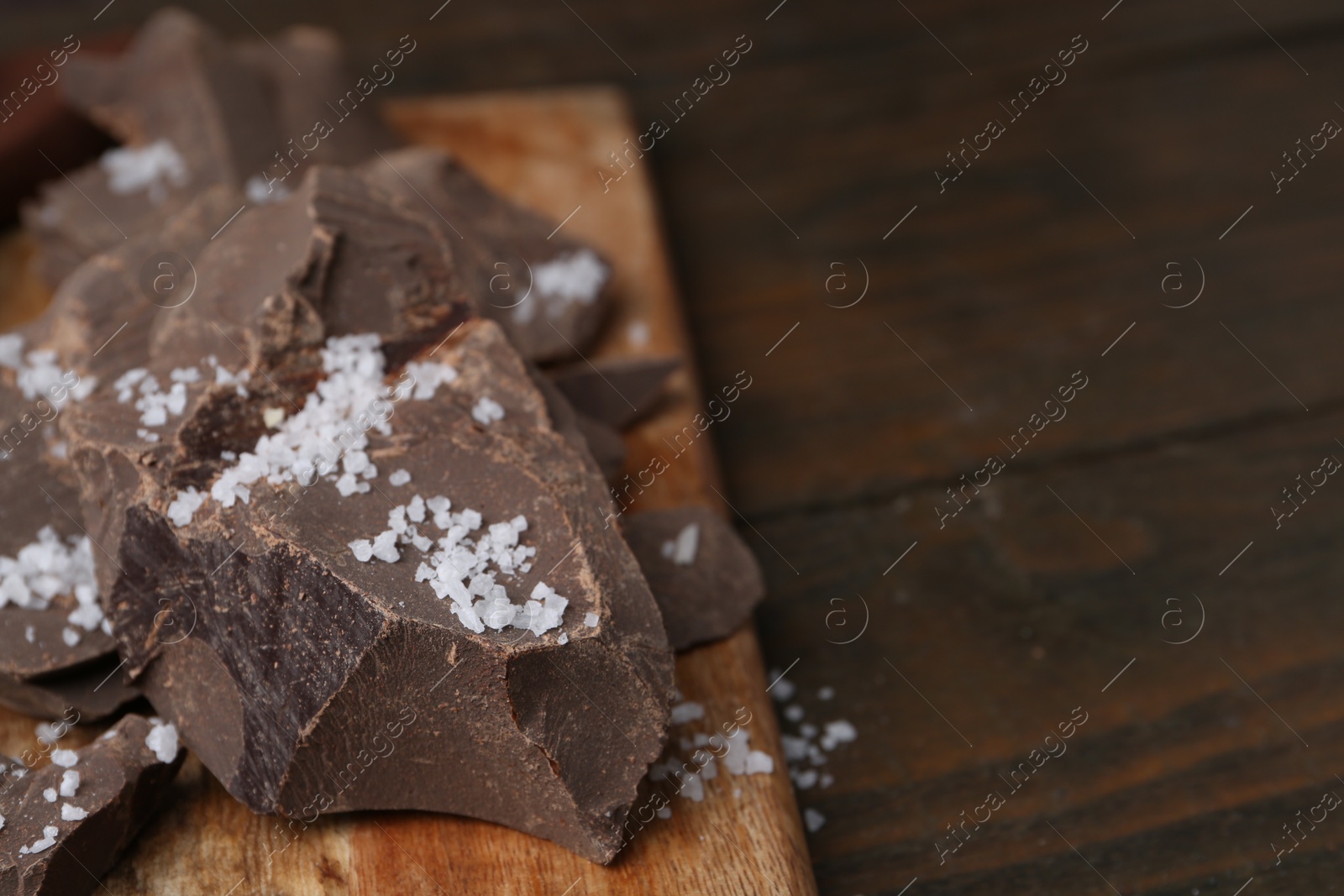 Photo of Pieces of chocolate with salt on wooden table, closeup. Space for text