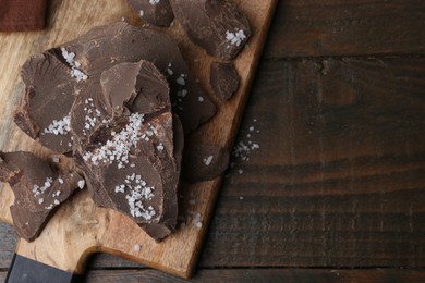 Photo of Pieces of chocolate with salt on wooden table, above view. Space for text