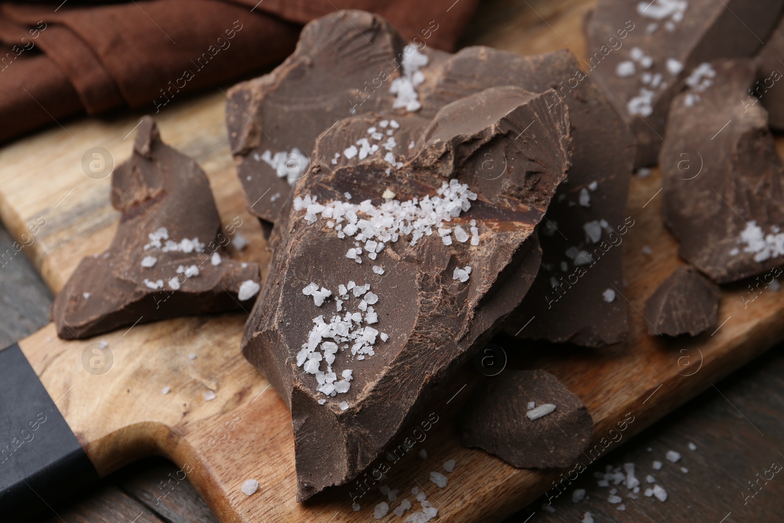 Photo of Pieces of chocolate with salt on wooden table, closeup