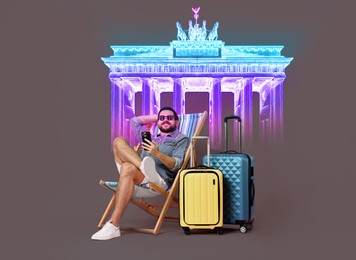 Happy traveler with suitcases and mobile phone sitting on deckchair against dark grey background. Neon illustration of Brandenburg gate behind man