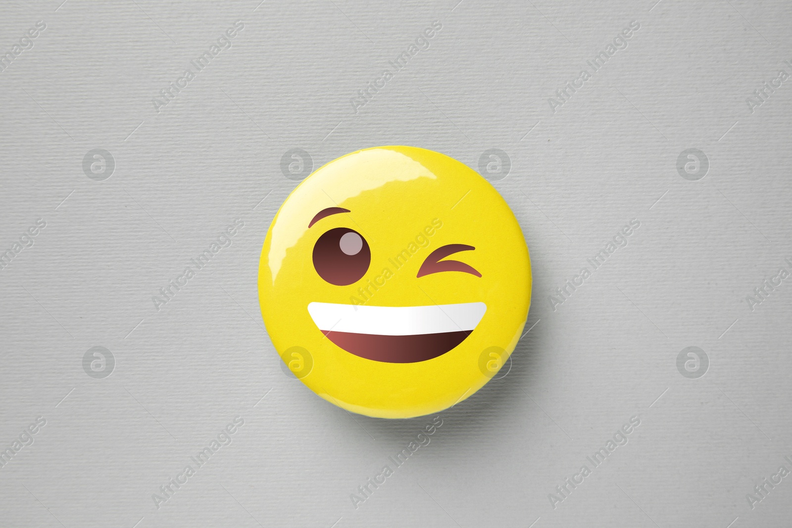 Image of Badge displaying face with winking eye on grey background