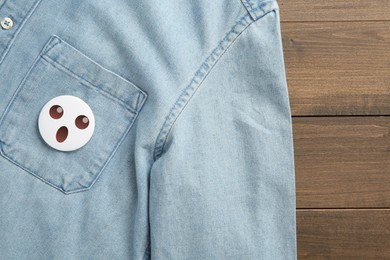 Image of Badge with shocked of surprised face attached to pocket of denim shirt on wooden background, top view