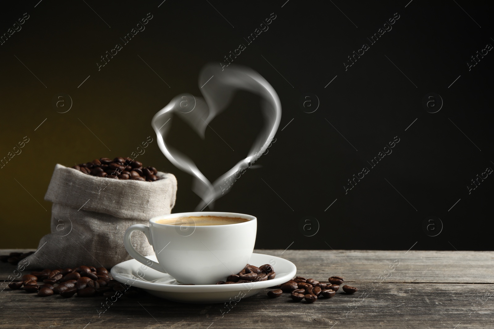 Image of Fresh aromatic coffee and beans on wooden table, space for text. Steam in shape of heart over cup