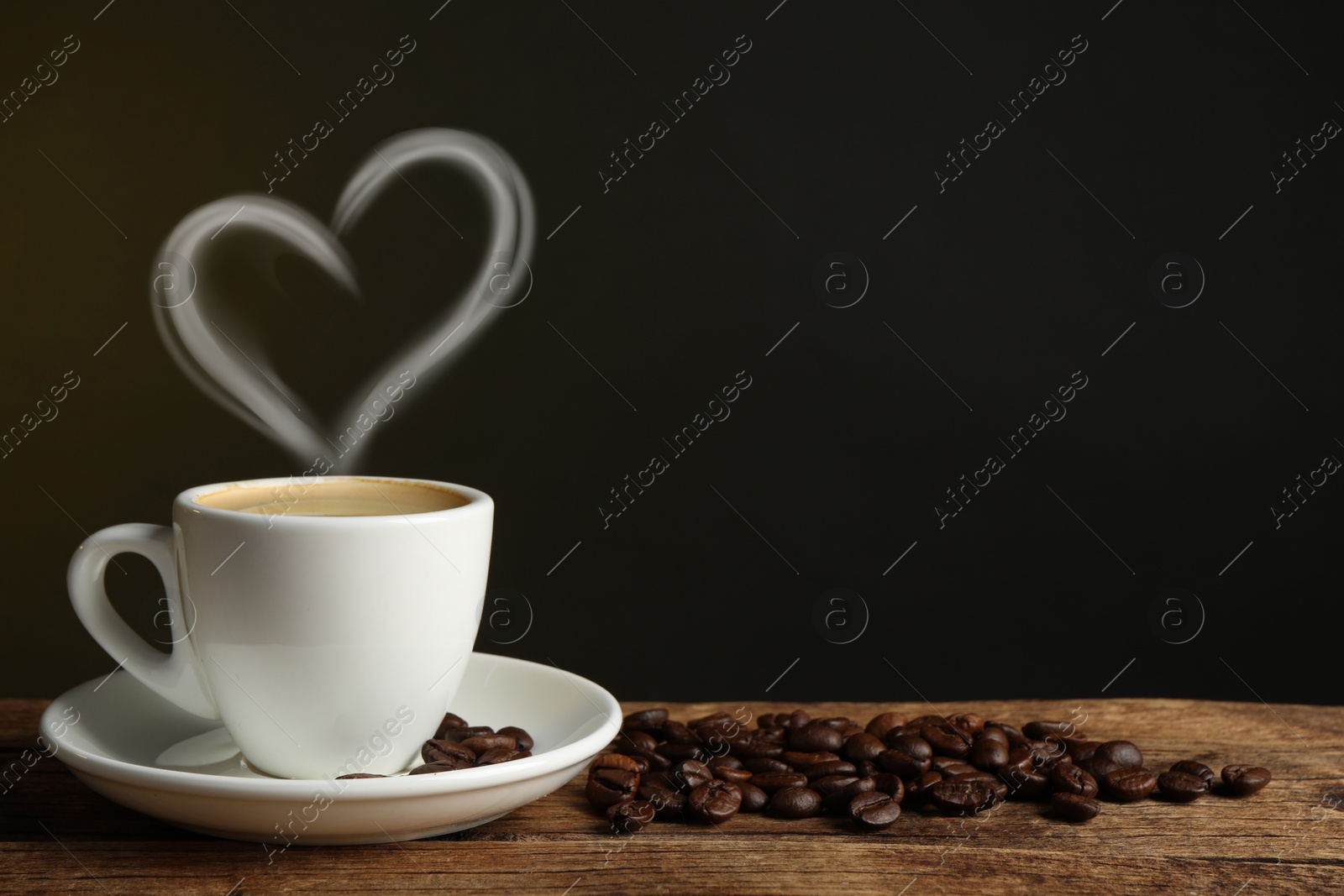 Image of Fresh aromatic coffee and beans on wooden table, space for text. Steam in shape of heart over cup