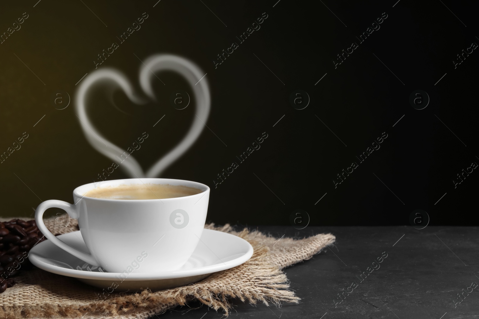 Image of Fresh aromatic coffee and beans on table, space for text. Steam in shape of heart over cup