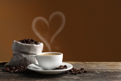 Image of Fresh aromatic coffee and beans on wooden table, space for text. Steam in shape of heart over cup