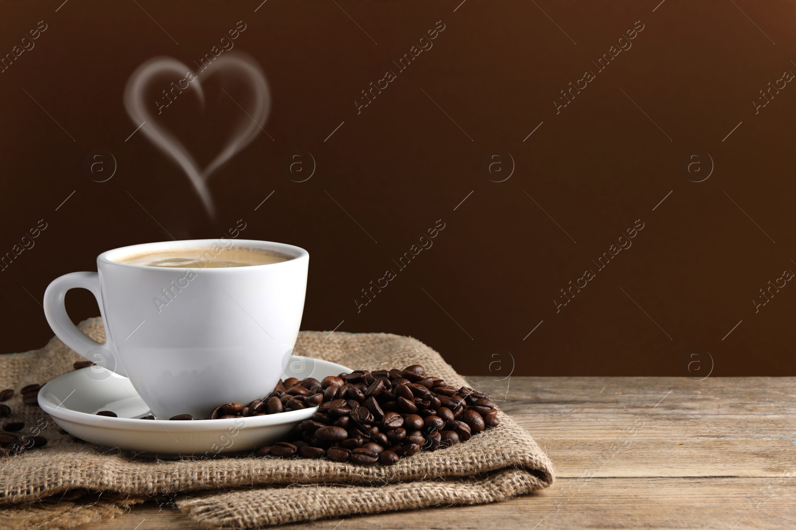 Image of Fresh aromatic coffee and beans on wooden table, space for text. Steam in shape of heart over cup