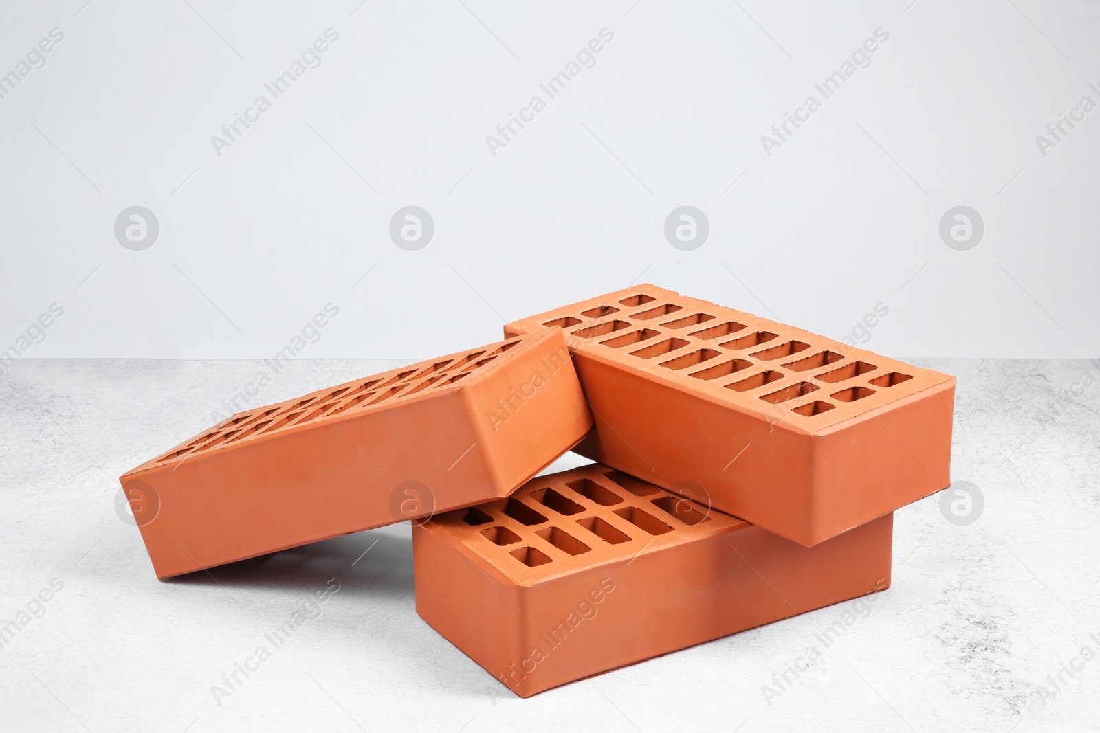 Photo of Three red bricks on textured table against light background. Building material