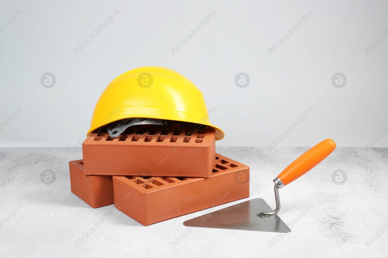 Photo of Red bricks, trowel and hard hat on textured table against light background