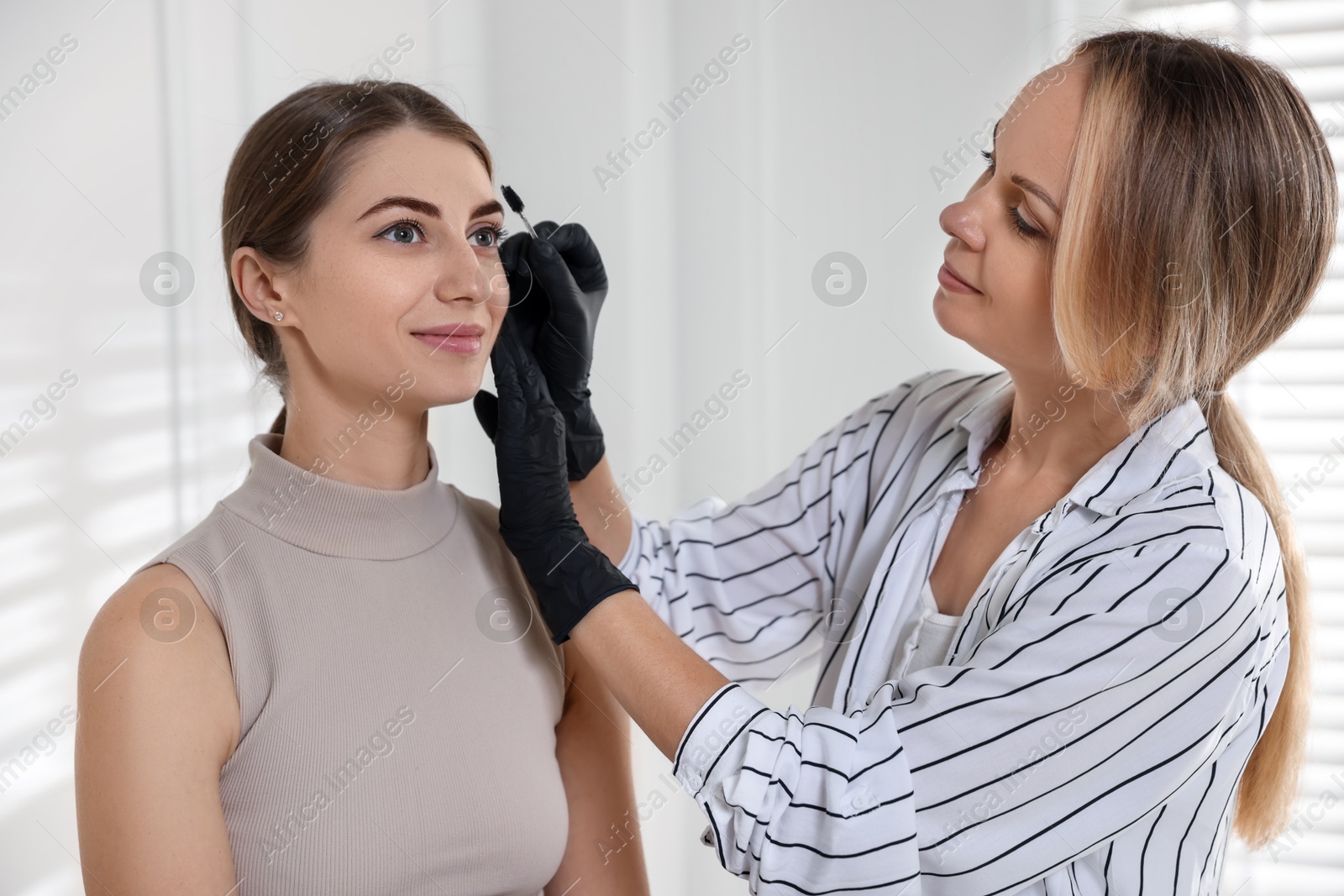 Photo of Beautician brushing client's eyebrows after henna dyeing procedure in salon