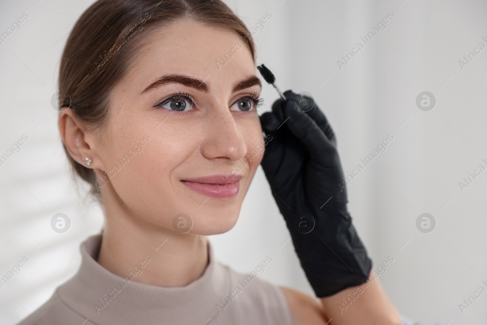 Photo of Beautician brushing client's eyebrows after henna dyeing procedure in salon, closeup