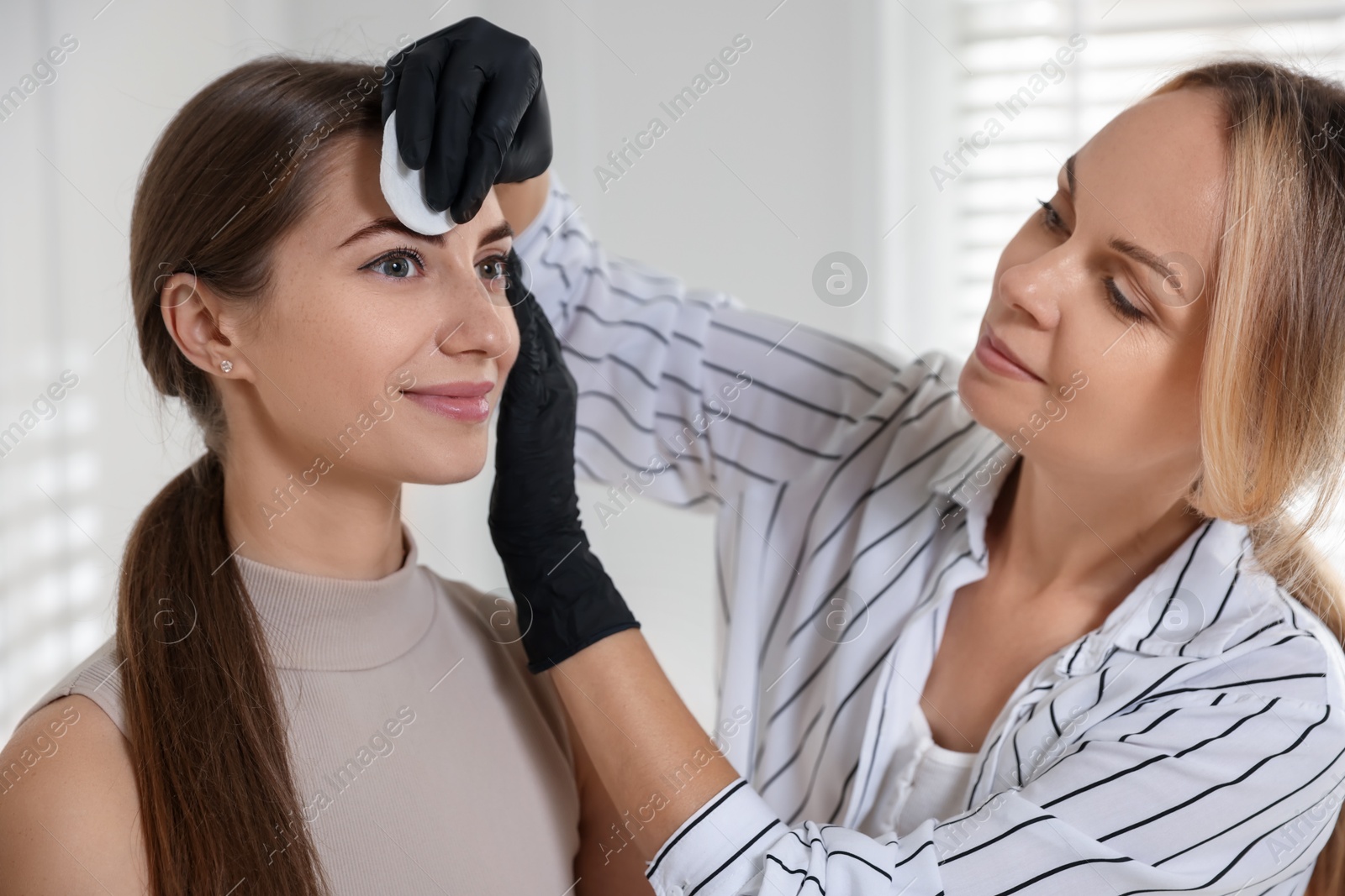 Photo of Beautician wiping client`s eyebrows after henna dyeing in salon