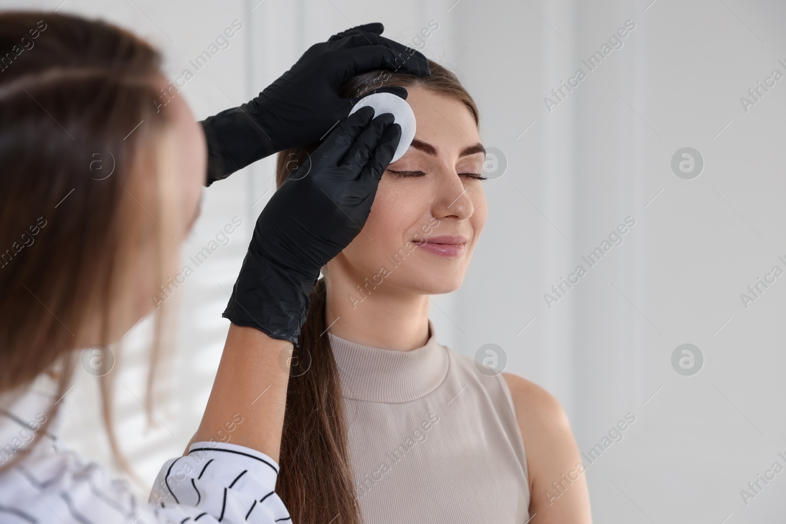 Photo of Beautician wiping client`s eyebrows after henna dyeing in salon