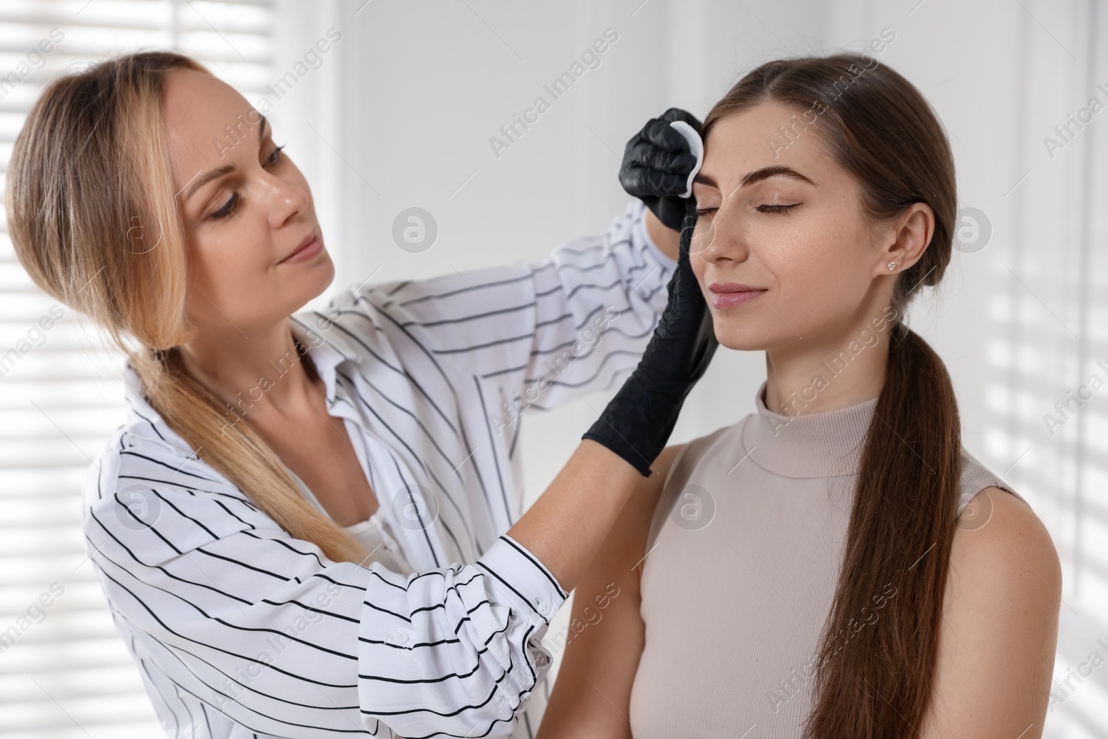 Photo of Beautician wiping client`s eyebrows after henna dyeing in salon