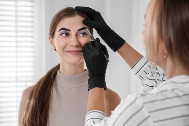 Photo of Beautician dyeing client’s eyebrows with henna in salon, closeup