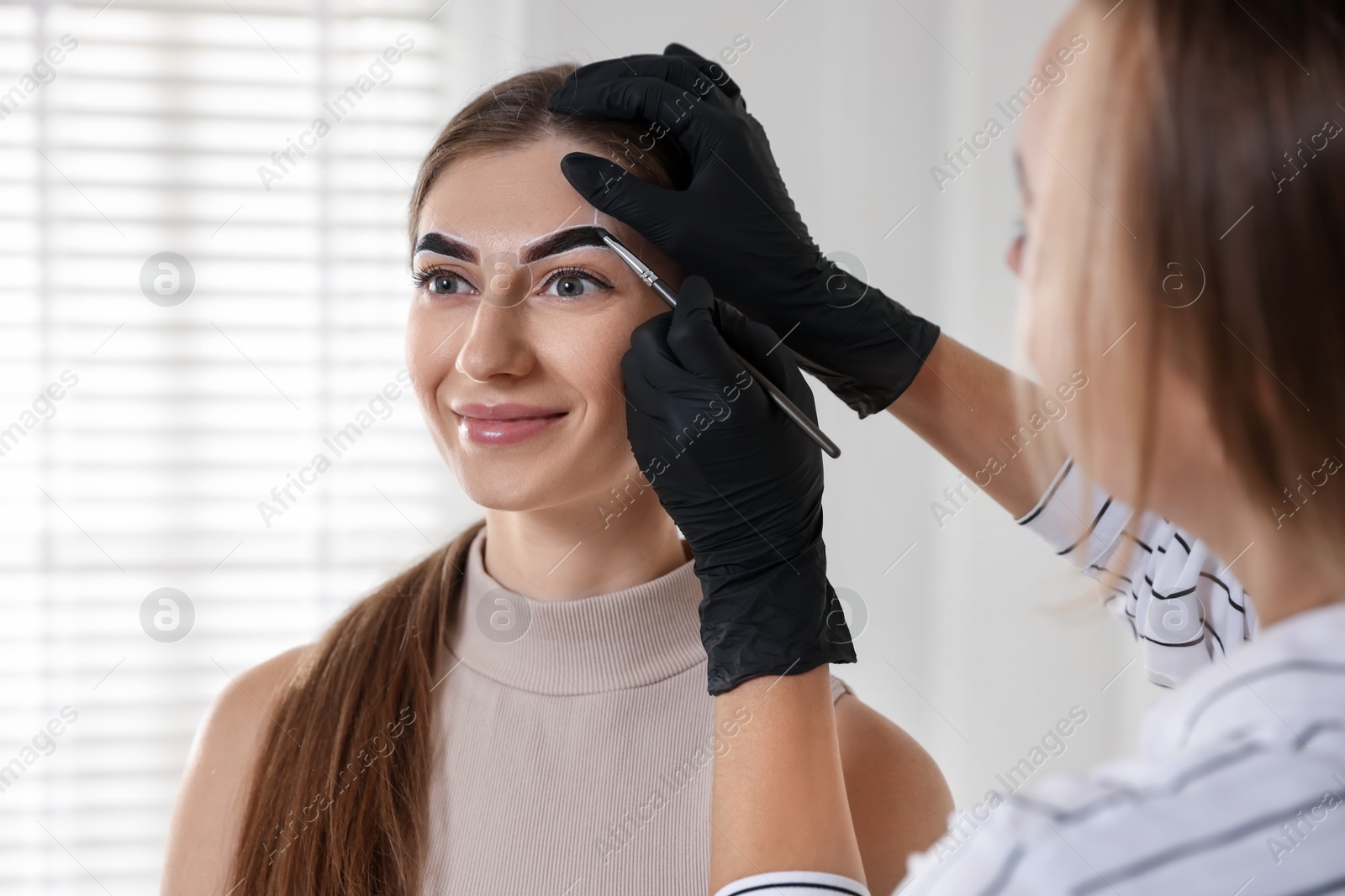 Photo of Beautician dyeing client’s eyebrows with henna in salon, closeup