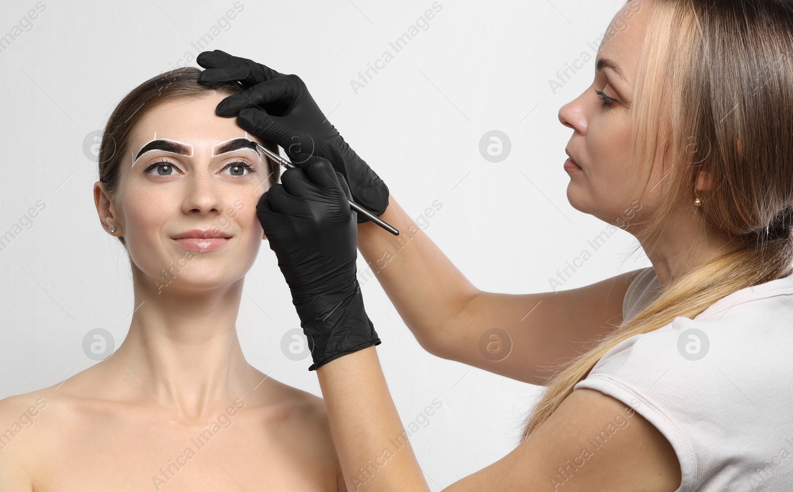 Photo of Beautician dyeing client’s eyebrows with henna on light background