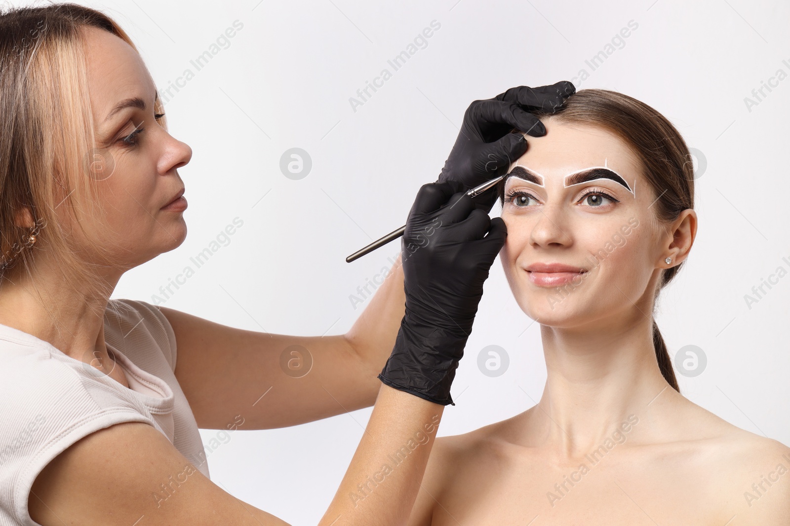 Photo of Beautician dyeing client’s eyebrows with henna on light background