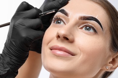 Young woman undergoing henna eyebrows dyeing procedure on light background, closeup