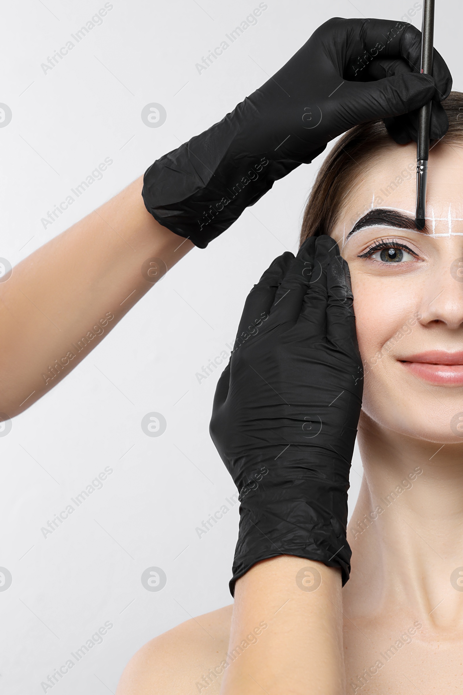 Photo of Young woman undergoing henna eyebrows dyeing procedure on light background, closeup