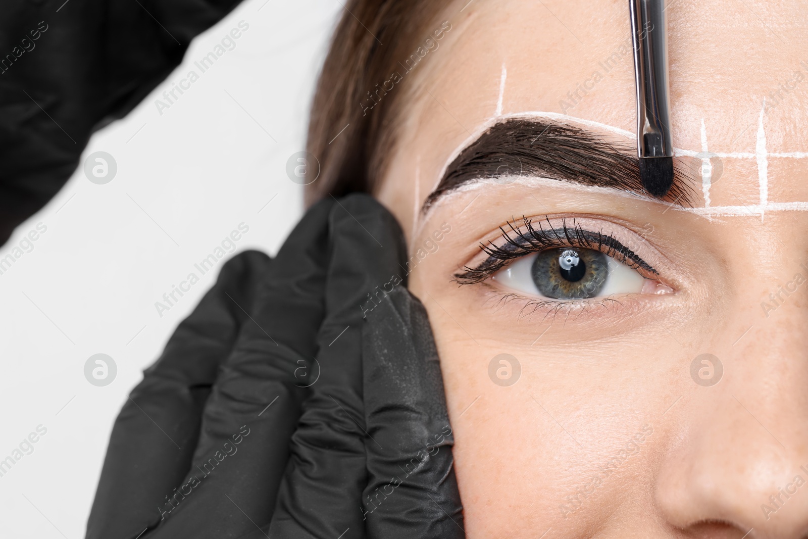 Photo of Young woman undergoing henna eyebrows dyeing procedure on light background, closeup