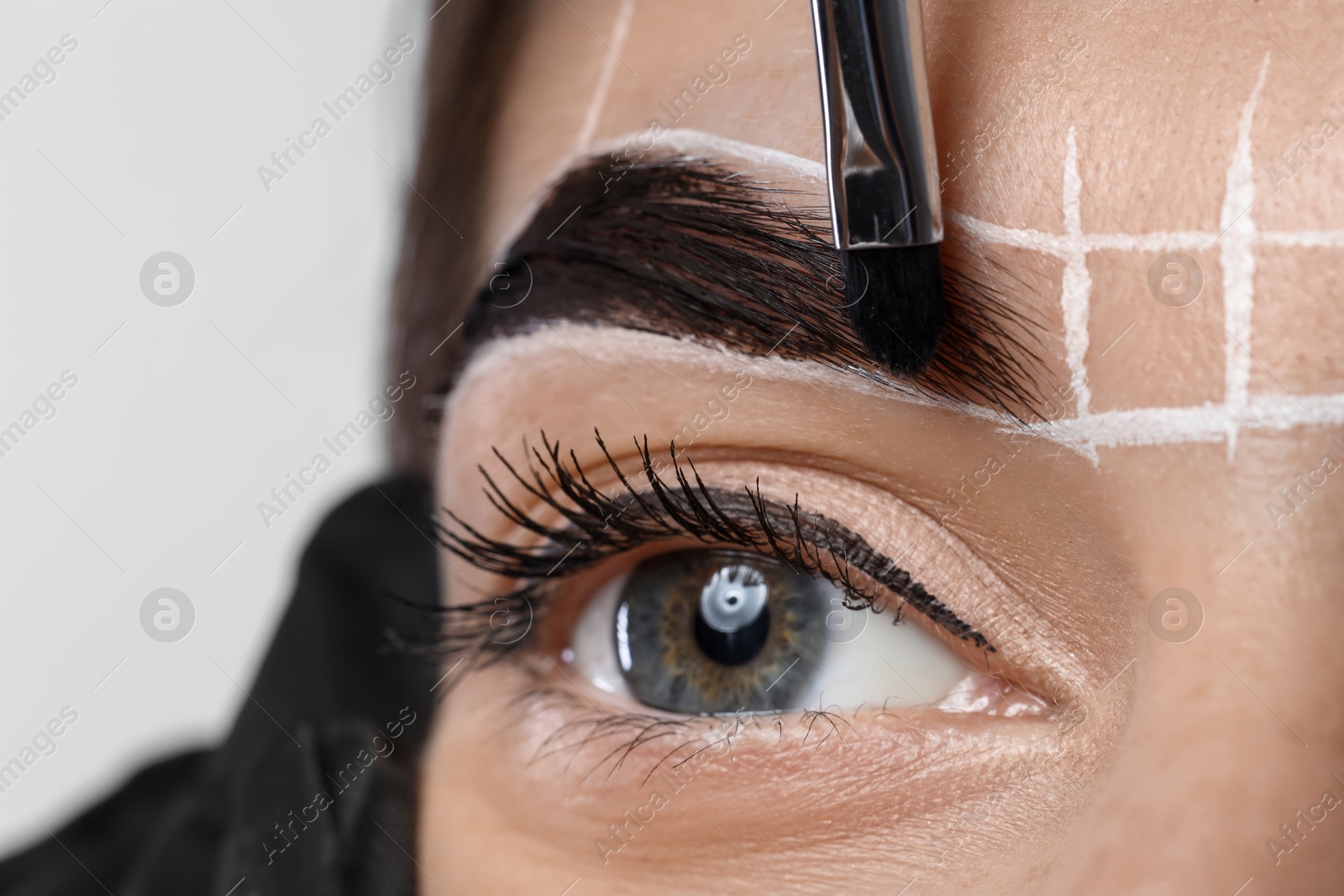 Photo of Young woman undergoing henna eyebrows dyeing procedure on light background, closeup