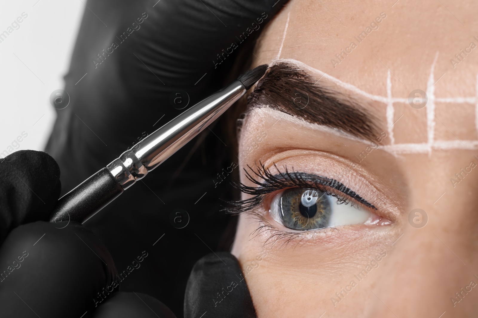 Photo of Young woman undergoing henna eyebrows dyeing procedure, closeup