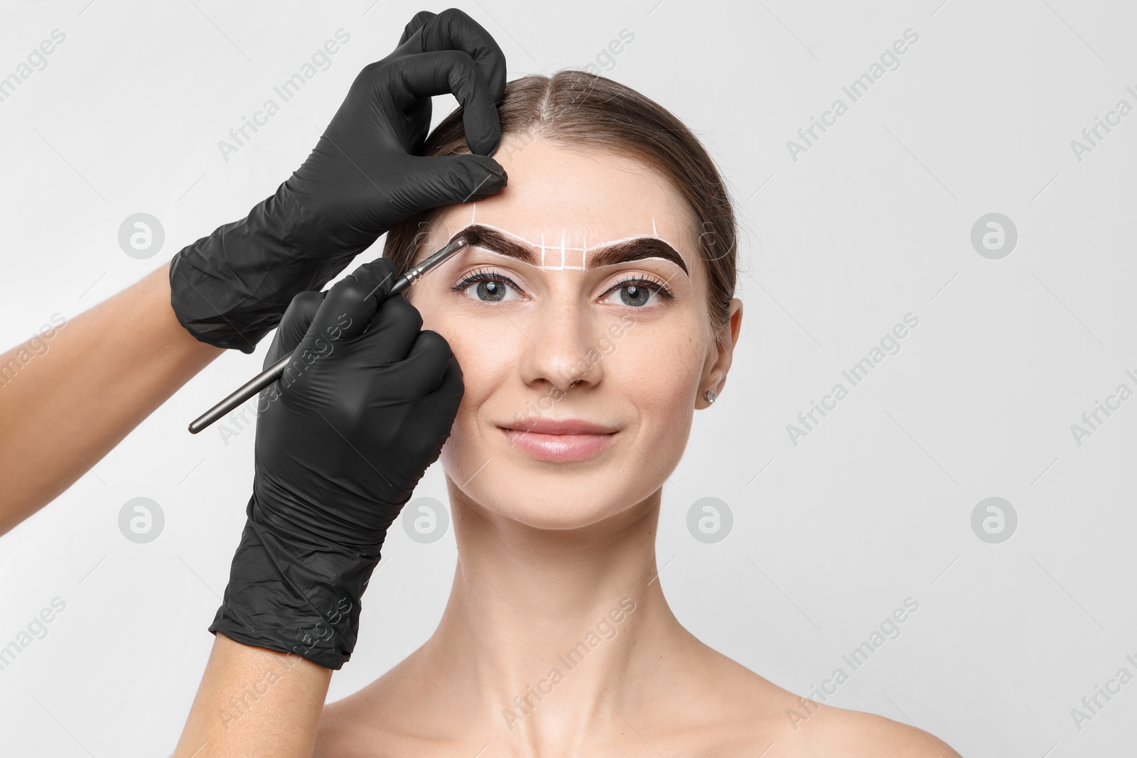 Photo of Young woman undergoing henna eyebrows dyeing procedure on light background, closeup