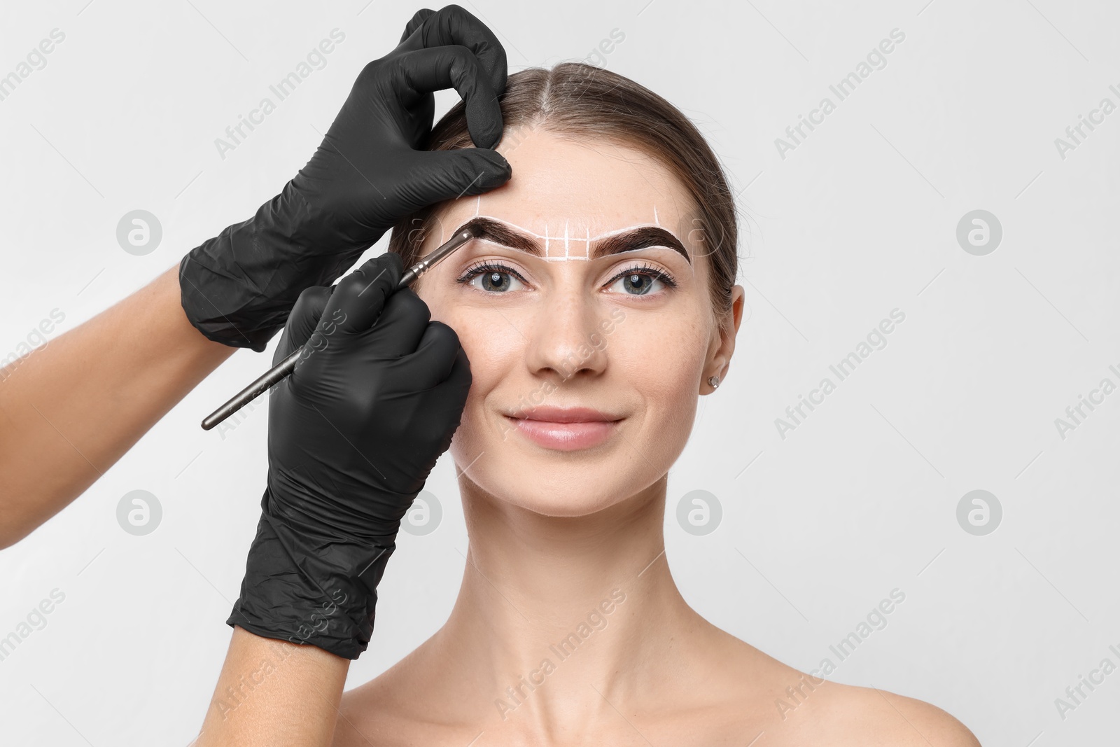 Photo of Young woman undergoing henna eyebrows dyeing procedure on light background, closeup