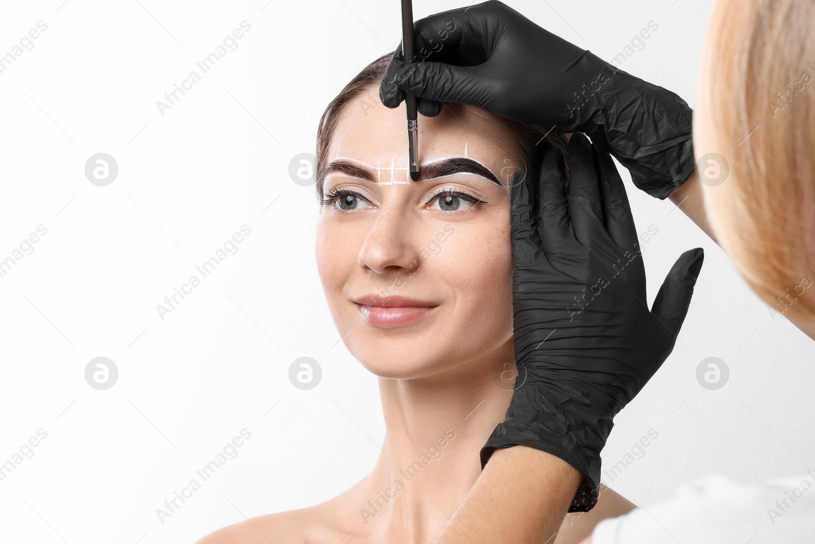 Photo of Young woman undergoing henna eyebrows dyeing procedure on white background