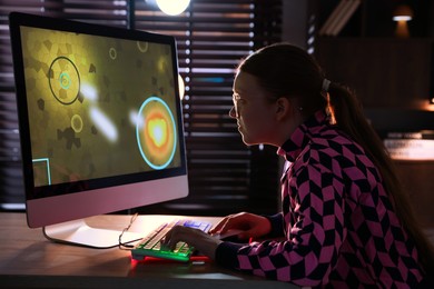 Girl playing video game with keyboard and mouse at table in dark room