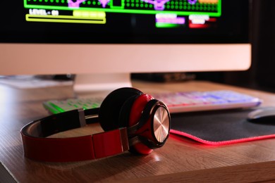 Photo of Headphones, computer keyboard and monitor on wooden table, closeup