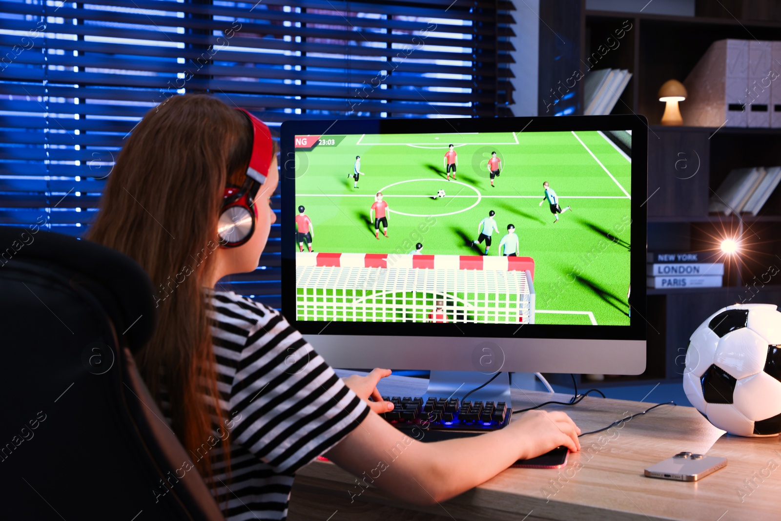 Photo of Girl playing video game with keyboard at table indoors, back view