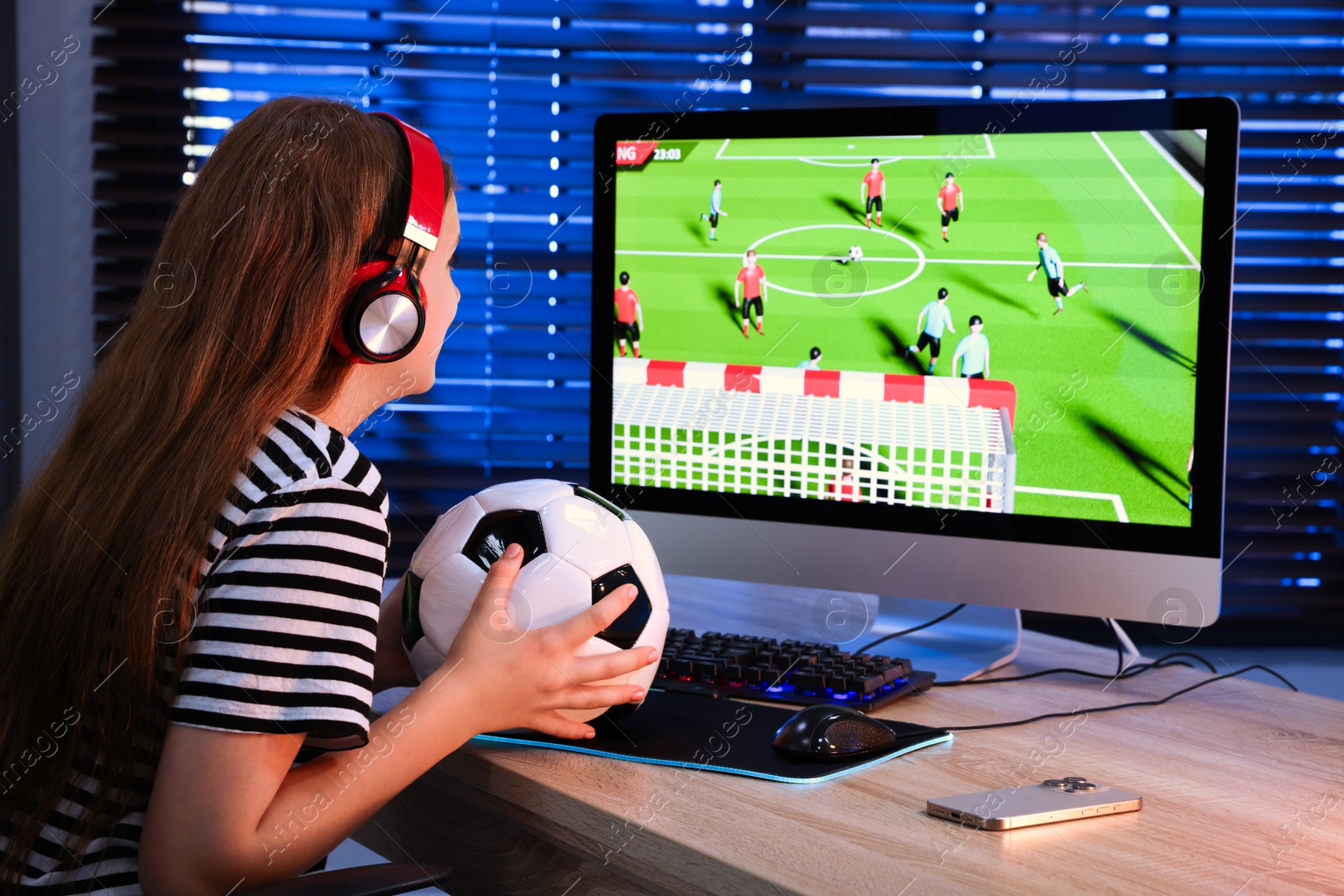 Photo of Football fan with soccer ball watching game live stream at table with computer keyboard, smartphone and mouse