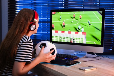 Photo of Football fan with soccer ball watching game live stream at table with computer keyboard, smartphone and mouse