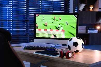 Photo of Computer keyboard, monitor, soccer ball, headphones and mouse on table indoors