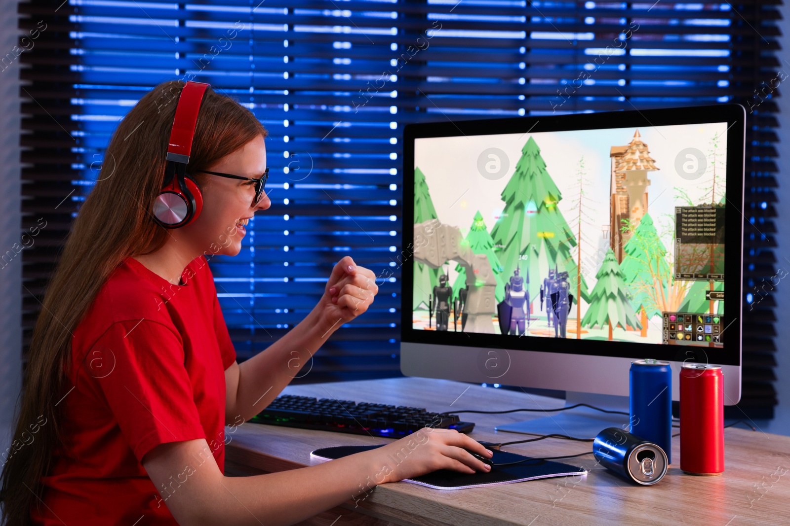 Photo of Happy girl playing video game with keyboard and mouse at table in dark room