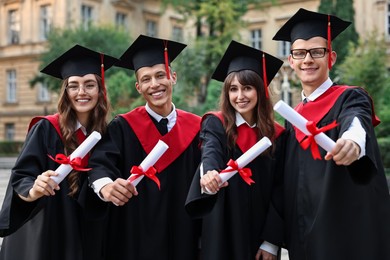 Happy students with diplomas after graduation ceremony outdoors