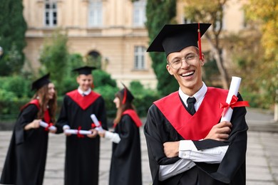 Photo of Happy students with diplomas after graduation ceremony outdoors, selective focus