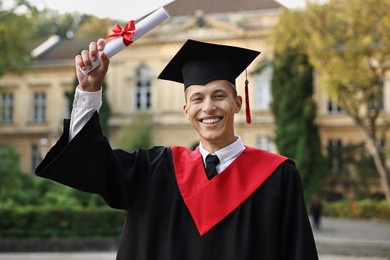 Photo of Happy student with diploma after graduation ceremony outdoors