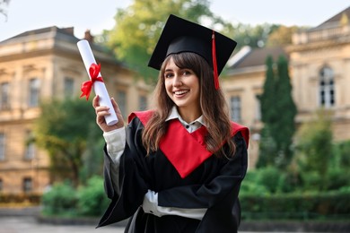 Photo of Happy student with diploma after graduation ceremony outdoors