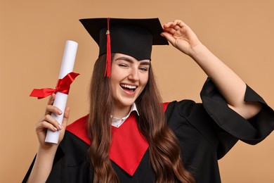 Happy student with diploma after graduation on beige background