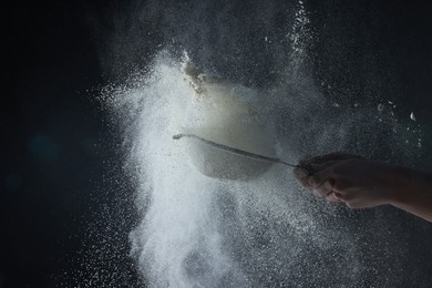 Photo of Woman throwing flour from sieve on black background, closeup