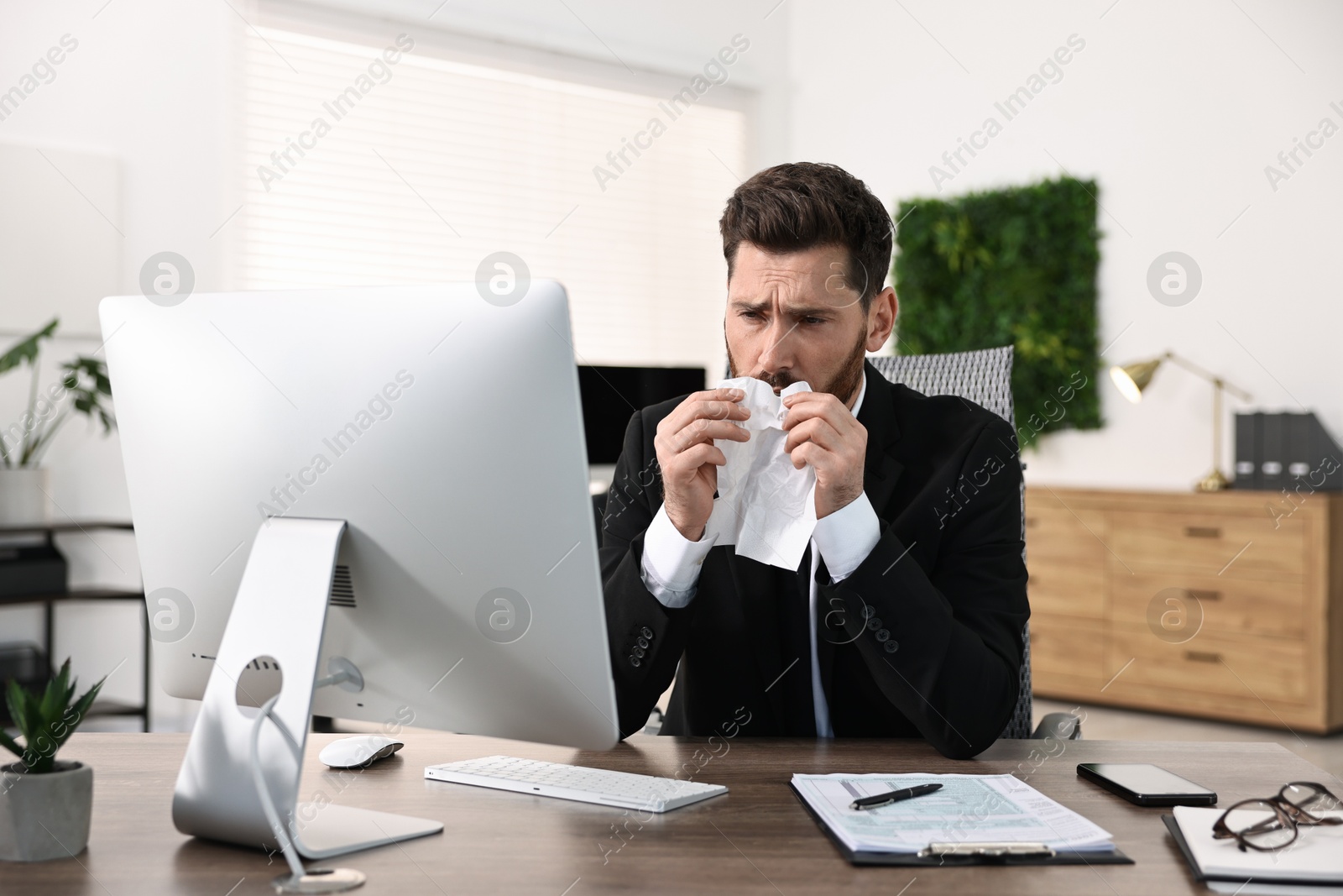 Photo of Sick man with runny nose at table in office