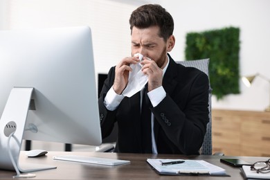 Photo of Sick man with runny nose at table in office